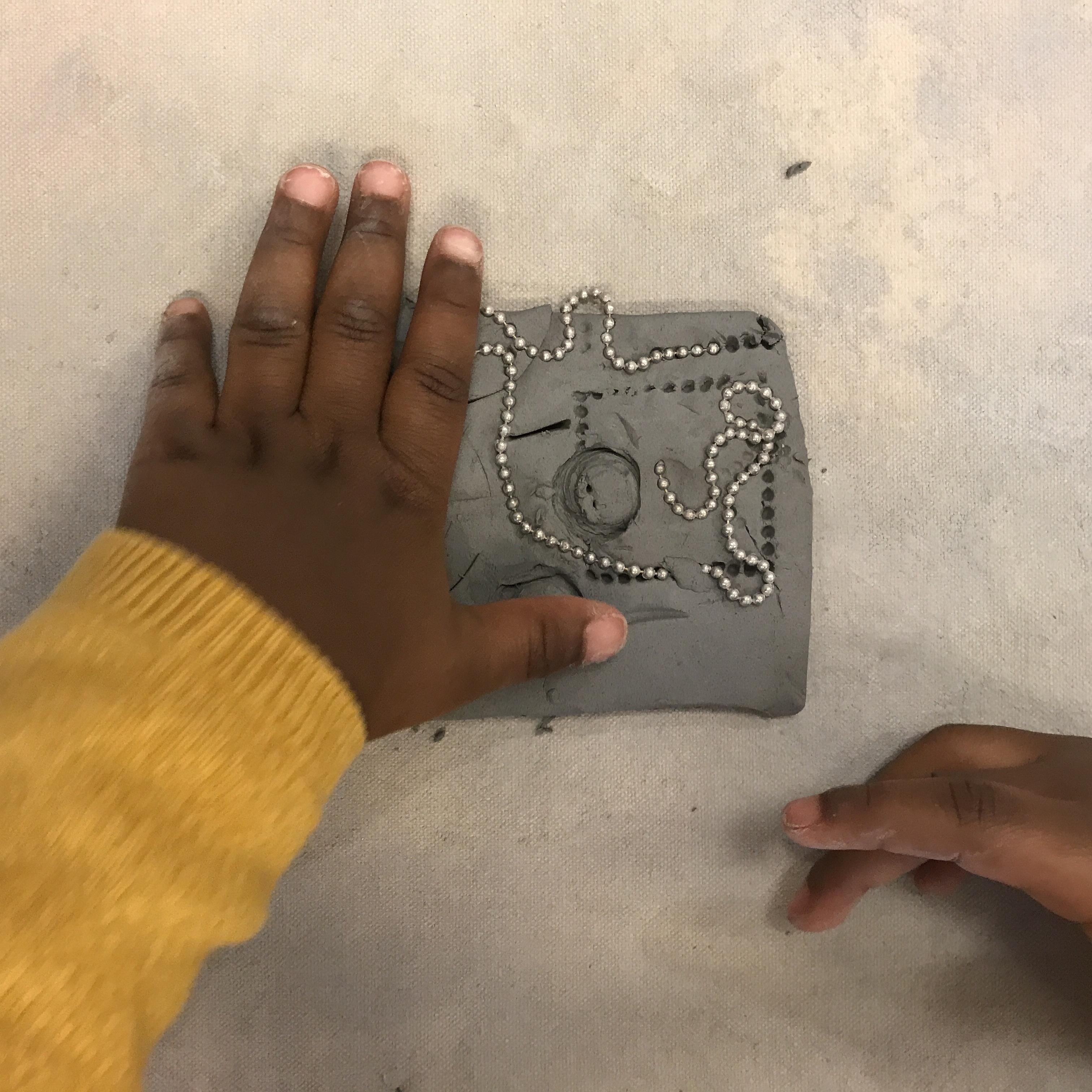 child's hands placing chain in clay