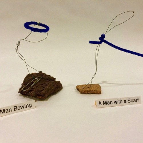 two wire figures one says 'man bowing' the other saying 'a man with a scarf'
